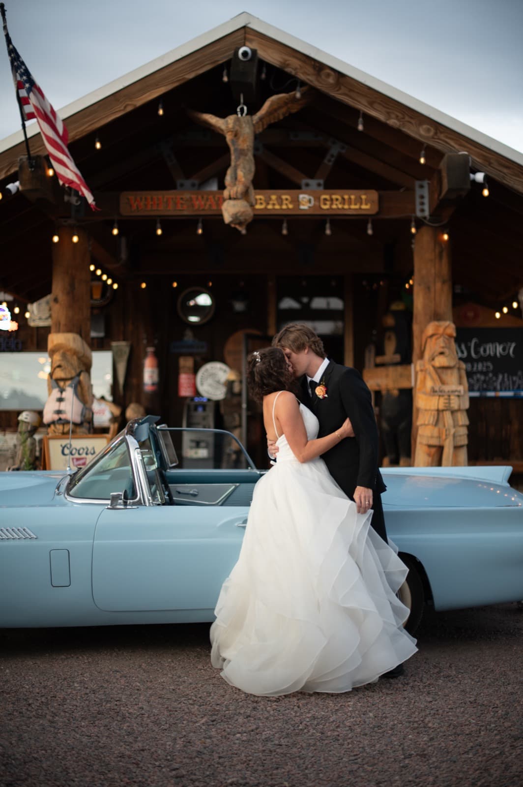 Newlyweds by vintage Thunderbird convertible at dusk