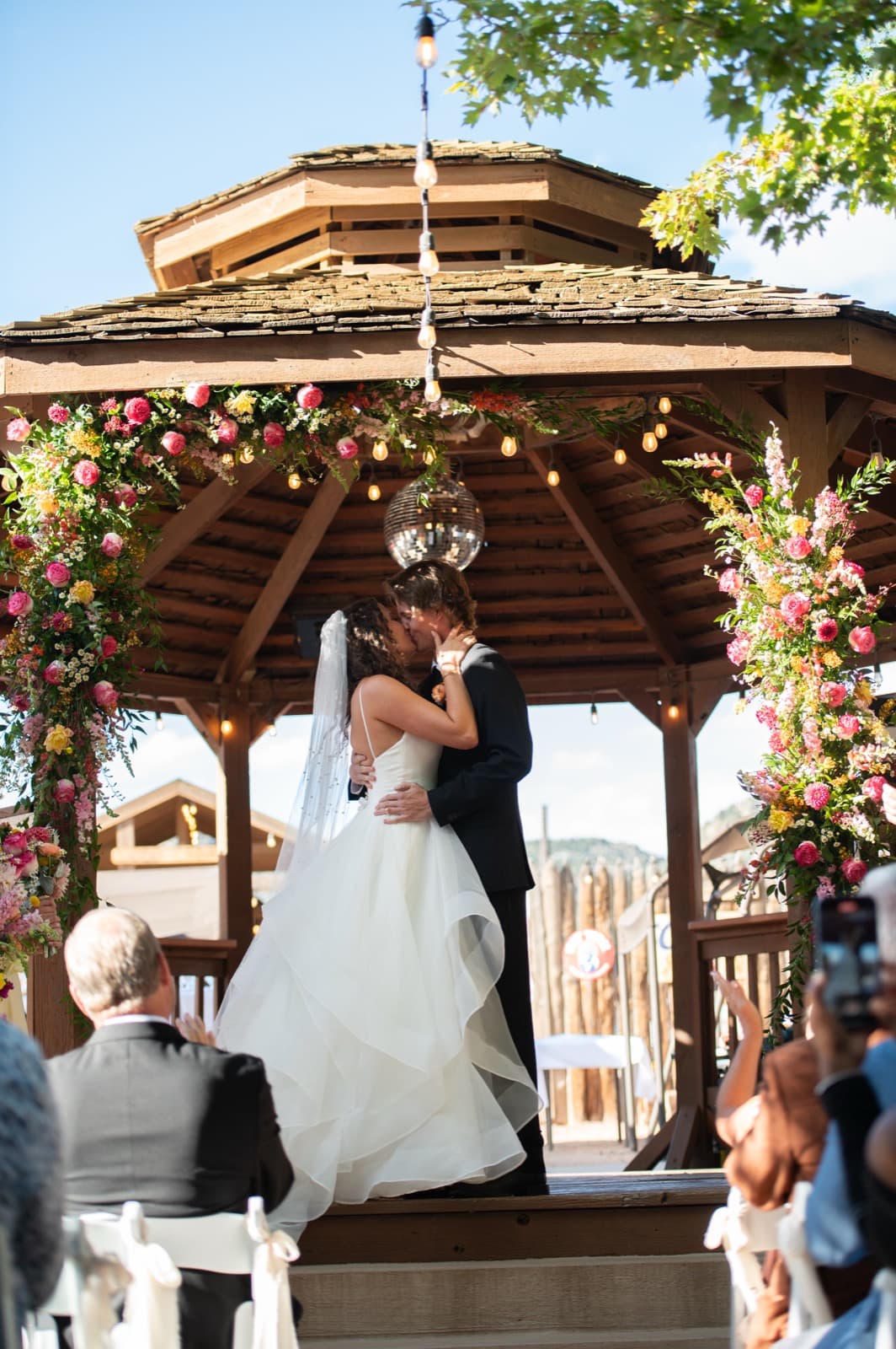 First kiss under the floral arch in the gazebo with mountain backdrop