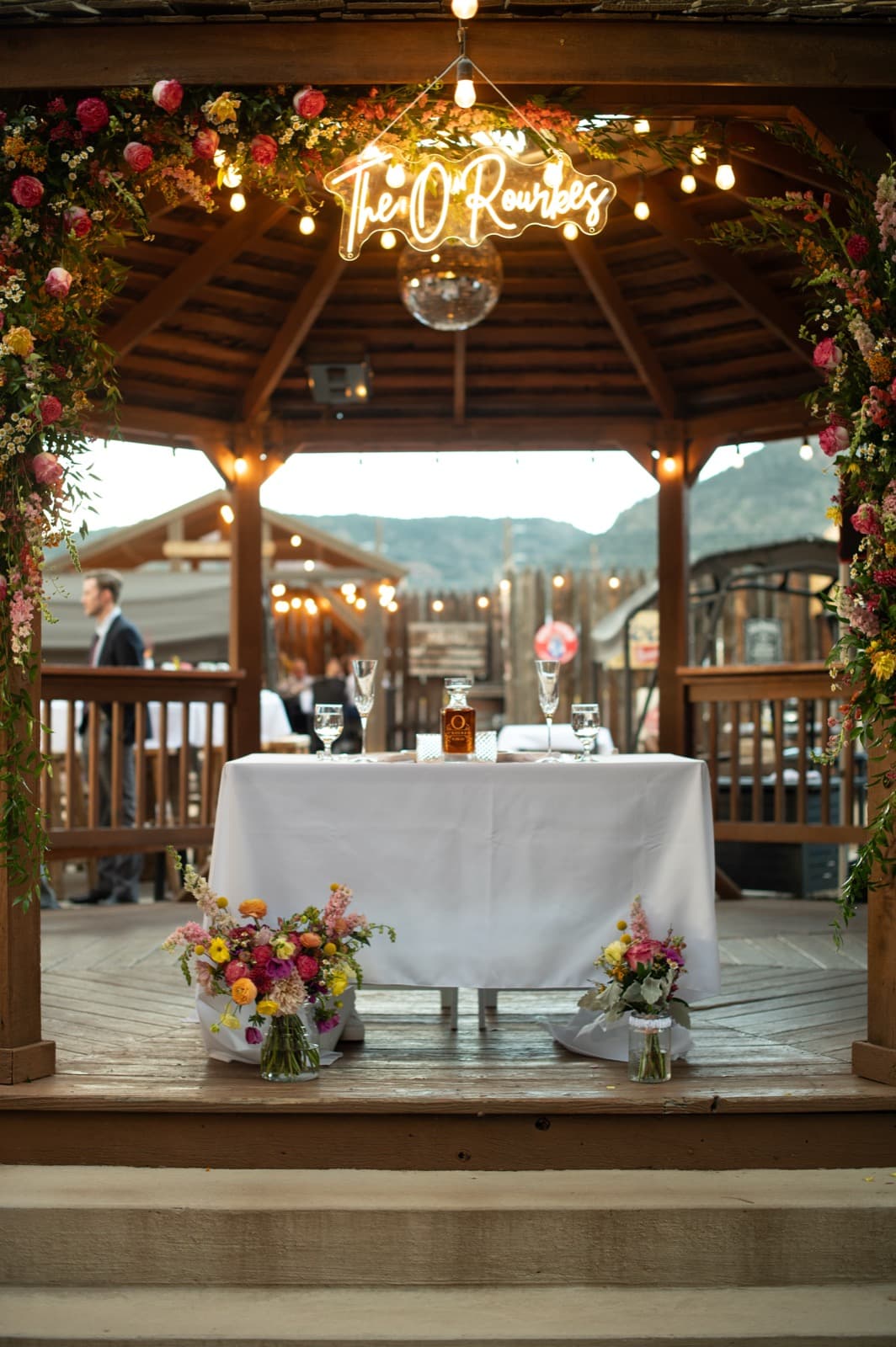 Sweetheart table with neon sign, gazebo, floral arch, and string lights